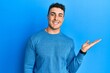 © Krakenimages.com - Hispanic young man wearing casual winter sweater smiling cheerful presenting and pointing with palm of hand looking at the camera.