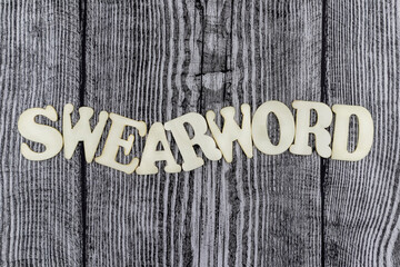 Fototapete - Swearword - concept design template on rustic wooden background with wavy line of alphabet letters and copyspace above and below