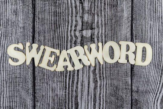 Swearword - concept design template on rustic wooden background with wavy line of alphabet letters and copyspace above and below
