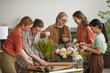 Diverse group of young florists arranging floral compositions while working in flower shop