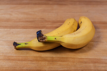 Two yellow banana fruit lying on wooden table surface.