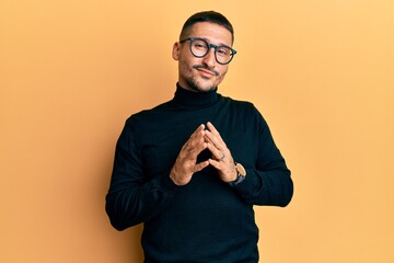 Poster - Handsome man with tattoos wearing turtleneck sweater and glasses hands together and fingers crossed smiling relaxed and cheerful. success and optimistic