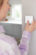 © Daisy Daisy - Woman At Home In Kitchen Turning Down Central Heating Thermostat To Save Energy And Money