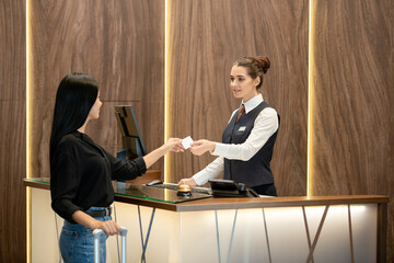 Aufkleber - Young brunette receptionist in uniform standing by workplace and passing plastic card to one of guests over reception counter in hotel lobby