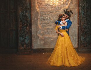 Couple embrace in room old castle. Happy beauty woman fantasy princess in yellow dress and guy is enchanted beast, horns on head. Romantic male prince hugs girl in arms. Man monster carnival costume.