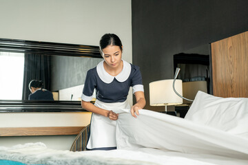 Poster - Young pretty brunette maid putting white clean blanket while changing bed in one of hotel rooms during preparation for new guests