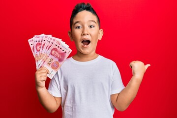 Sticker - Little boy hispanic kid holding yuan chinese banknotes pointing thumb up to the side smiling happy with open mouth