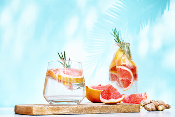 Wall Mural - Summer cocktail with grapefruit and rosemary and juicy slices citrus fruits. Fresh healthy grapefruit beverage on sunlight with shadows. Creative drink on blue pastel background.