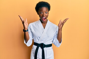 Poster - Young african american girl wearing karate kimono and black belt celebrating crazy and amazed for success with arms raised and open eyes screaming excited. winner concept