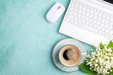 Home office desk table with coffee cup, bouquet of spring flowers lily of the valley flat lay. Workplace with laptop and coffee on green background. Blogging, freelance, florist concept. Сopy space