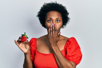 Wall Mural - Young african american woman holding strawberry covering mouth with hand, shocked and afraid for mistake. surprised expression