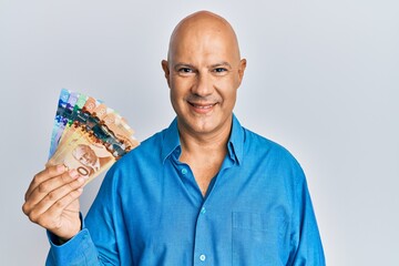 Wall Mural - Middle age bald man holding canadian dollars looking positive and happy standing and smiling with a confident smile showing teeth