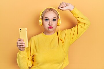 Canvas Print - Young blonde woman dancing wearing headphones puffing cheeks with funny face. mouth inflated with air, catching air.