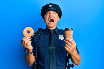 Wall Mural - Handsome middle age mature police man eating donut and drinking coffee angry and mad screaming frustrated and furious, shouting with anger looking up.