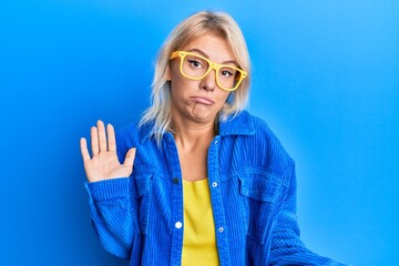 Sticker - Young blonde girl wearing casual clothes and glasses clueless and confused expression with arms and hands raised. doubt concept.