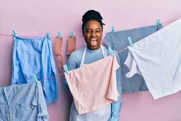 Wall Mural - African american woman with braided hair washing clothes at clothesline sticking tongue out happy with funny expression. emotion concept.