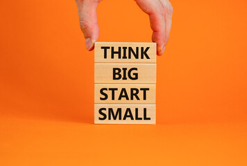 Wall Mural - Think big start small symbol. Concept words 'Think big start small' on wooden blocks on a beautiful orange background. Businessman hand. Business, motivational and think big start small concept.