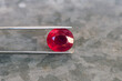 Deep saturated red natural mined Madagascar ruby, corundum - Al2O3 gemstone. Heated, treated, lead glass filled. Holded in tweezers. Clarity - Si,I2. Background - gray metal zinc pattern. For jewelry.