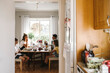 © Maskot - Happy family eating breakfast seen through doorway of kitchen at home