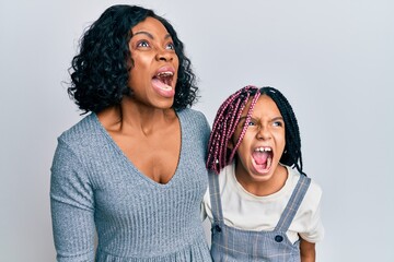 Sticker - Beautiful african american mother and daughter wearing casual clothes and hugging angry and mad screaming frustrated and furious, shouting with anger. rage and aggressive concept.