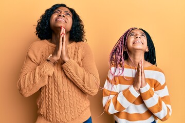 Poster - Beautiful african american mother and daughter wearing wool winter sweater begging and praying with hands together with hope expression on face very emotional and worried. begging.