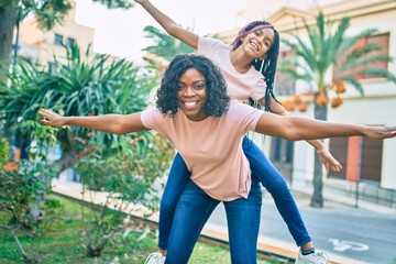 Sticker - Beautiful african american mother giving daughter piggyback ride with open arms at the park.