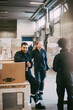 © Maskot - Male entrepreneur sitting on box container by colleagues at distribution warehouse