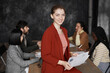 © Seventyfour - Waist up portrait of successful young businesswoman wearing red jacket and smiling at camera with diverse group of people meeting in background, copy space