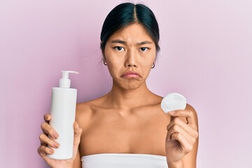 Poster - Young chinese woman wearing shower towel using clean lotion depressed and worry for distress, crying angry and afraid. sad expression.