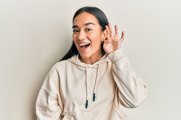 Poster - Young asian woman wearing casual sweatshirt smiling with hand over ear listening and hearing to rumor or gossip. deafness concept.