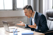 © Kateryna - Displeased confused bewildered gray-haired caucasian business leader or employee, frustrated looks at the laptop, received a bad message or news while sitting at the workplace, gesturing hands