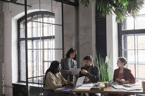 Fototapeta na szkło Wide angle view at multi-ethnic group of business people discussing project while sitting at meeting table in graphic office interior, copy space