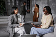 © Seventyfour - Portrait of two ethnic businesswomen discussing project while sitting in lounge area at modern office