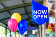 © Adam Calaitzis - A blue sign with the words NOW OPEN is hanging next to three balloons to advertise an open business