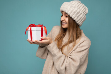 Shot of attractive positive smiling young dark blonde woman isolated over colourful background wall wearing everyday trendy outfit holding gift box and looking to the side