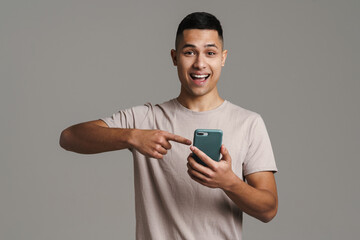 Brunette young excited man holding and pointing finger at mobile phone