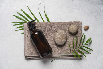 Spa cosmetic product on white stone background. Natural cosmetic in glass bottle with dispenser , towel and green plants for spa, home relaxation