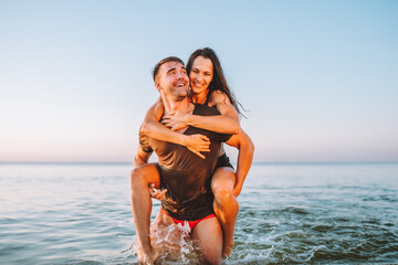 Happy young fit couple embrace each other with love in the sea or ocean at summer sunset. Romantic mood, tenderness, relationship, vacation concept.