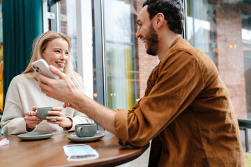 Sticker - Smiling man and woman talking and using cellphone while drinking coffee