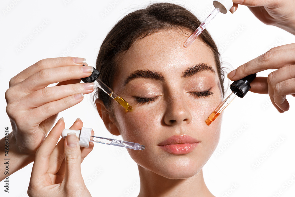 Skin care and rejuvenation. Beautiful Model With Radiant And Glowing Facial Skin Looking At Camera. Moisturizing With Serum Collagen And Hyaluronic Acid. Hands with serum dropper near girl face Stock Photo |