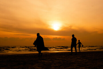 A silhouette of a monk and two people walking on the beach in Hua Hin, Thailand