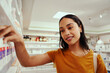 © StratfordProductions - Young smiling woman in casual clothing buying medicine in a pharmacy