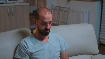Poster - Tired man sitting in front of television writing lifestyle information for online project on laptop. Caucaisan male lying on sofa late at night in kitchen using modern technology wireless