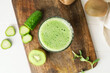 Glass of tasty green smoothie and ingredients on light wooden background, closeup