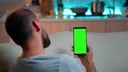 Poster - Caucasian male reading online social information on phone with mock up green screen chroma key display. Tired man sitting on sofa using isolated smartphone with technology internet