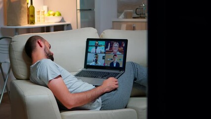 Poster - Tired man in pajamas sitting on sofa falling asleep while having online business videocall with teammates using laptop computer. Caucasian male on conference internet web communication