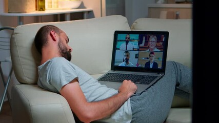 Poster - Comfortable man in pajamas falling asleep while chatting with collegues during online business videocall using laptop computer. Caucasian male sitting on couch late at night in kitchen