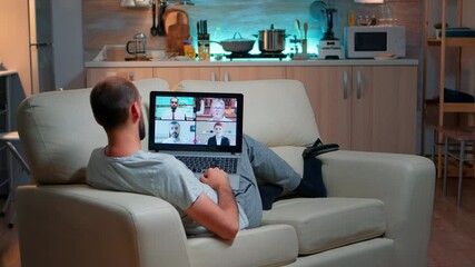 Poster - Caucasian male talking with collegues during video call conference using laptop computer with modern technology wireless. Tired man relaxing on sofa late at night in kitchen