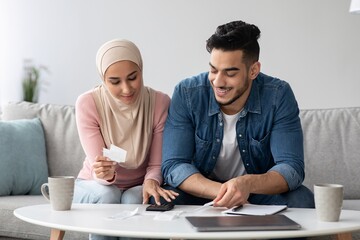 Wall Mural - Smiling man and woman in hijab working on family budget