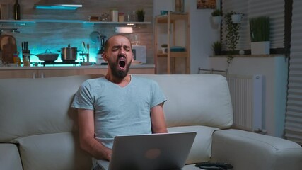 Poster - Focused man browsing information on network using laptop computer sitting in front of television. Caucaisan male lying on sofa late at night in kitchen using modern technology wireless